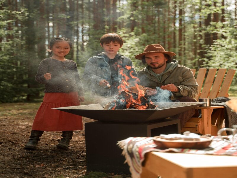 Een man en twee kinderen roosteren marshmellows in het bos op een camping in de meivakantie.